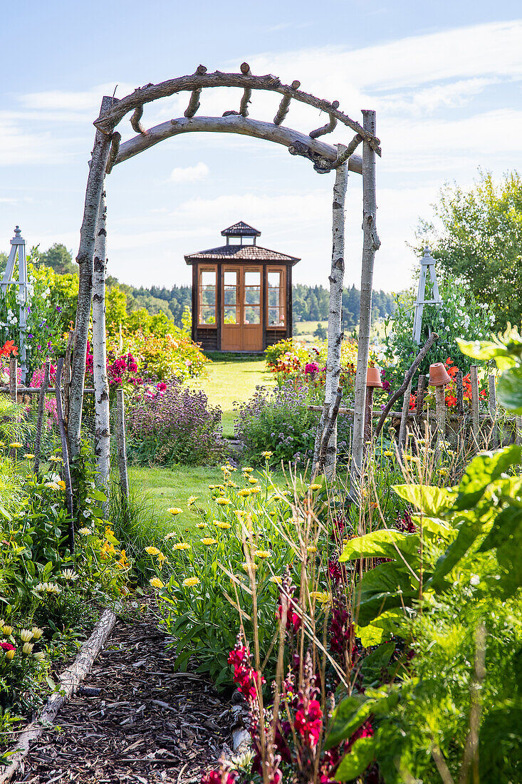 Gemüsegarten mit Portal, im Hintergrund Pavillon im Garten