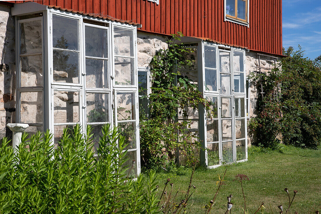 Small greenhouses made from old window frames against a natural stone house wall