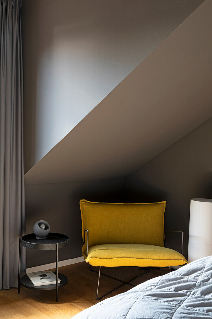 Gelber Polstersessel und Beistelltisch unter Dachschräge im Schlafzimmer