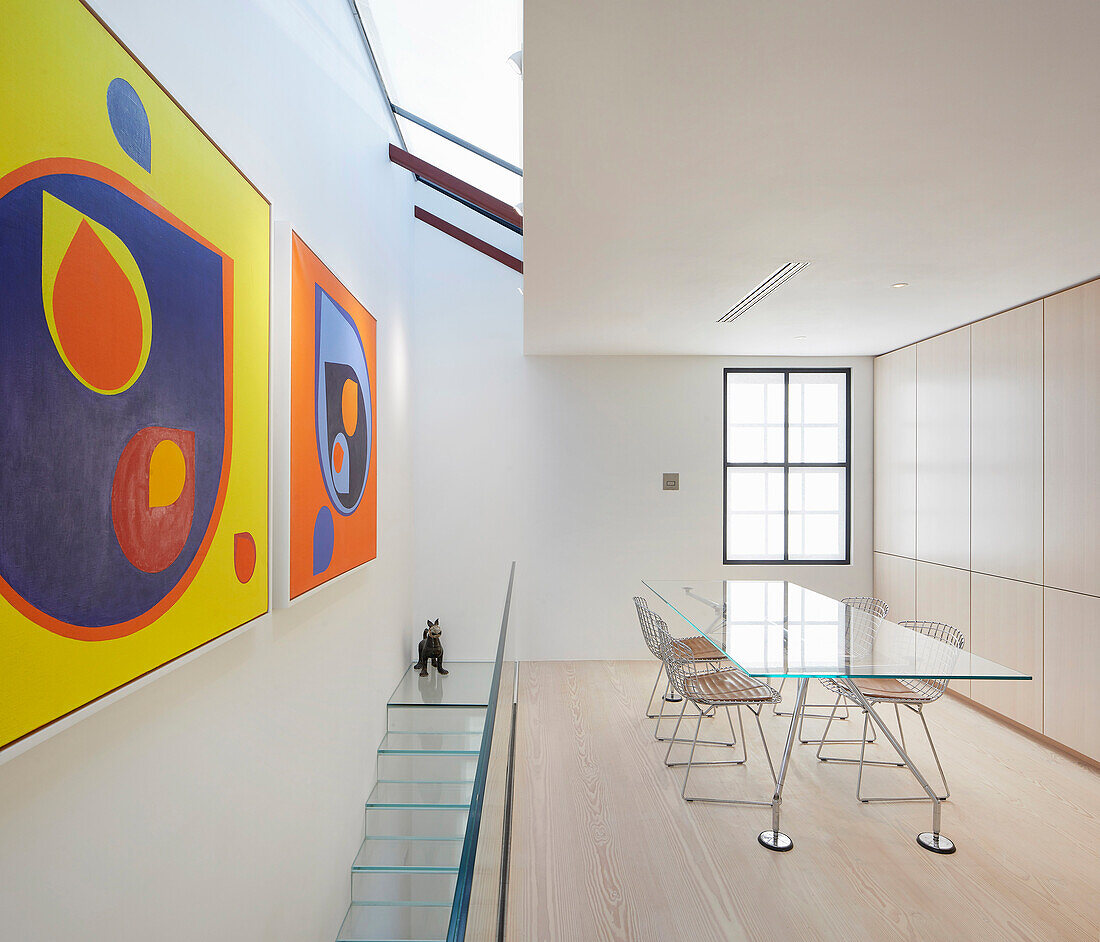 Glastisch mit Stühlen im Obergeschoss mit Oberlicht und moderner Kunst