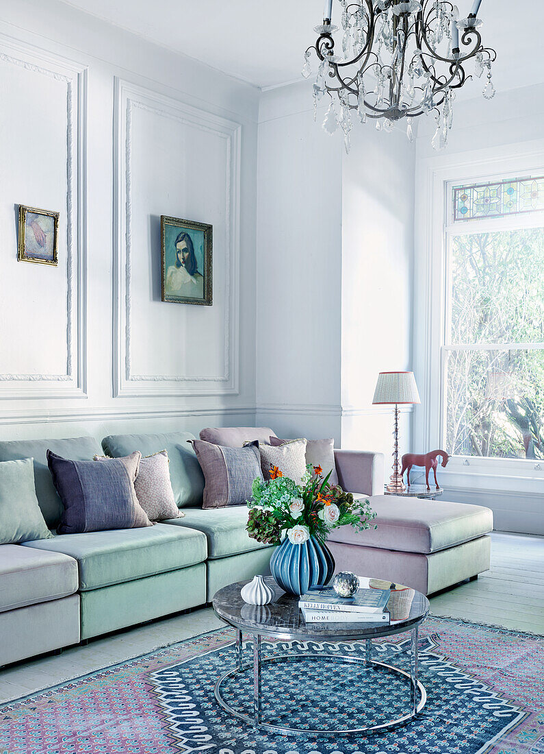 Weißes Wohnzimmer mit zweifarbigem Sofa, Kissen und Couchtisch mit Blumenarrangement
