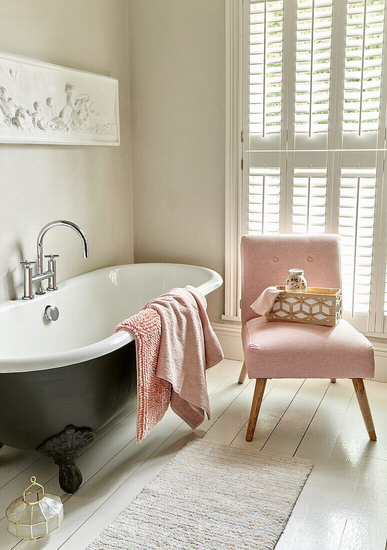 Bathroom with freestanding bathtub and pink upholstered chair