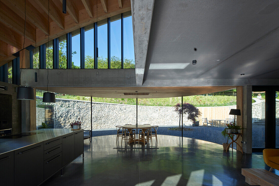 Offene Küche und Essbereich mit Betonboden im Architektenhaus mit gebogenem Dach