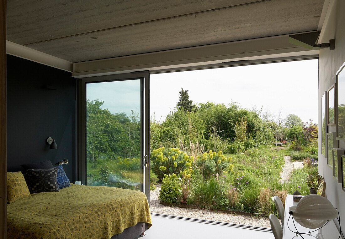Queen bed with yellow bedspread in a bedroom with a garden view through open glass sliding door