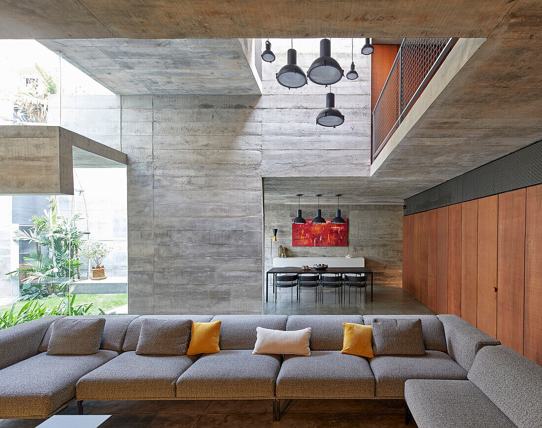 Open living room with sofa set and view to dining room in a concrete house