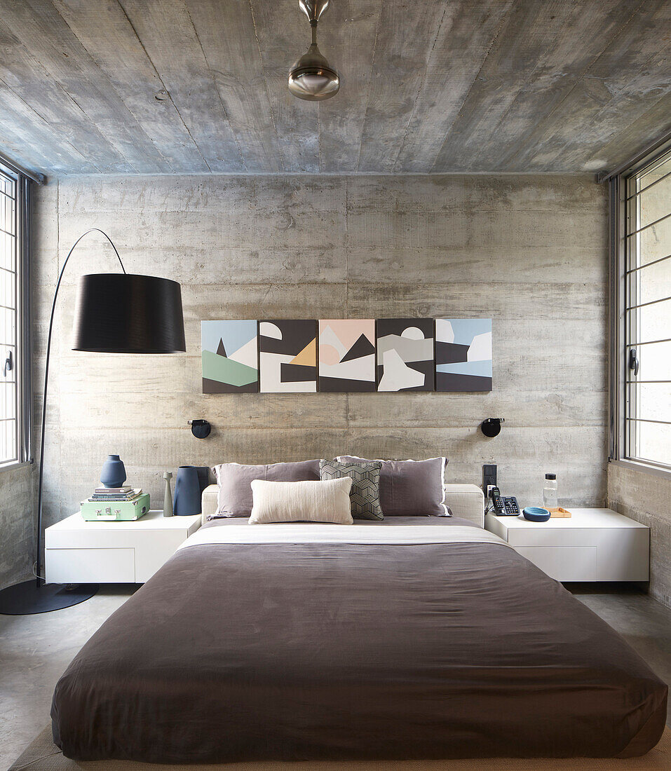 Schlafzimmer mit Doppelbett, darüber moderne Kunst an Betonwand