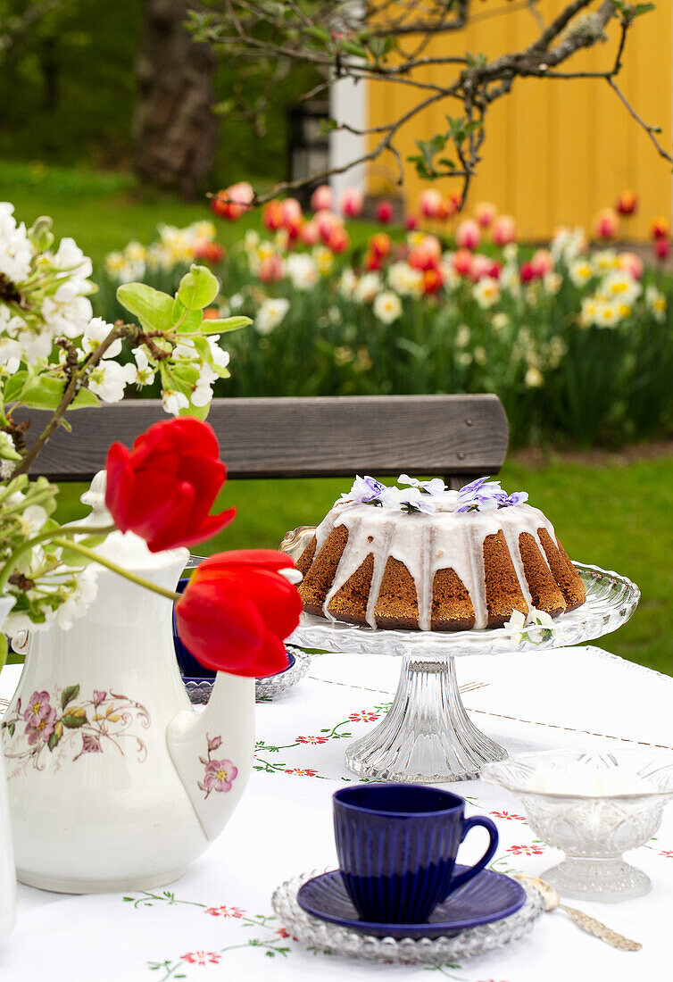 Table setting with cake, tea pot and bouquet of flowers in the spring garden