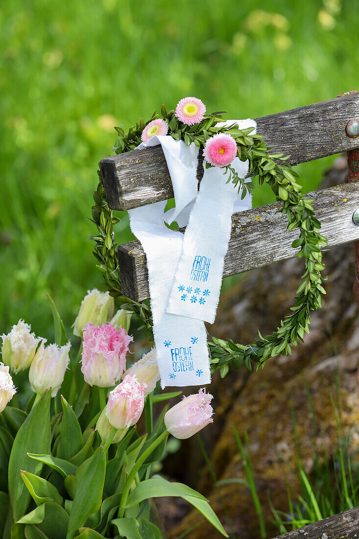 Wooden bench with wreath and daisies (Bellis), stamped fabric remnants with Easter greeting and tulips (Tulipa)