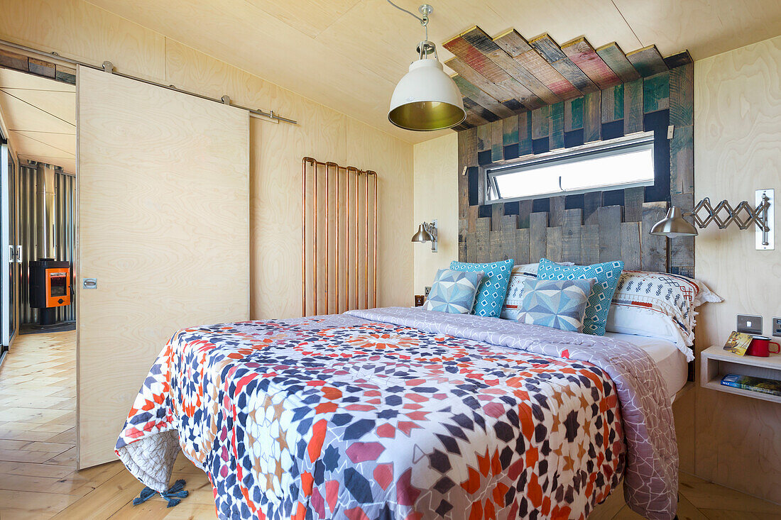 Colorful bedspread on double bed, headboard made of wooden boxes