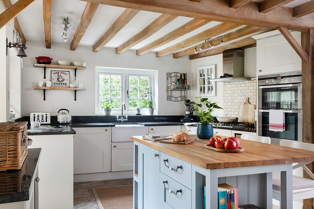 Country kitchen with light grey kitchen island and wooden beamed ceiling