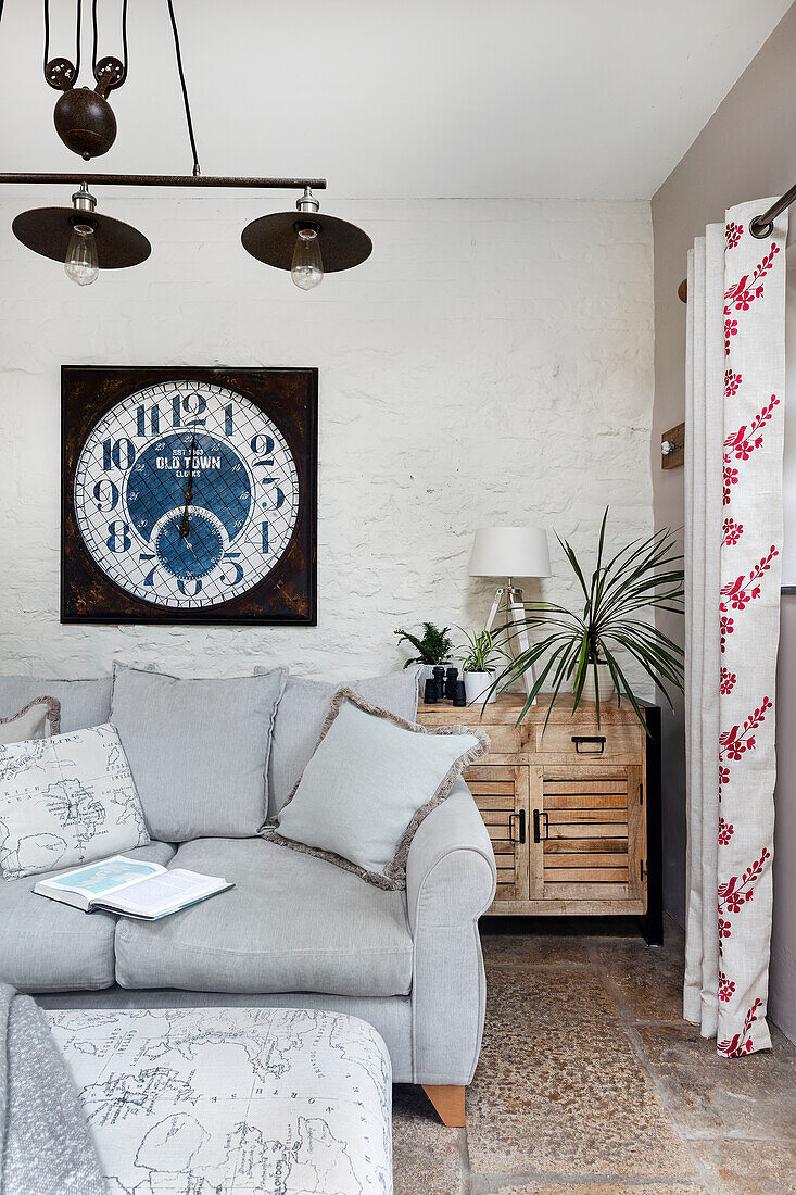 Cozy grey upholstered sofa with wall clock in the garden room
