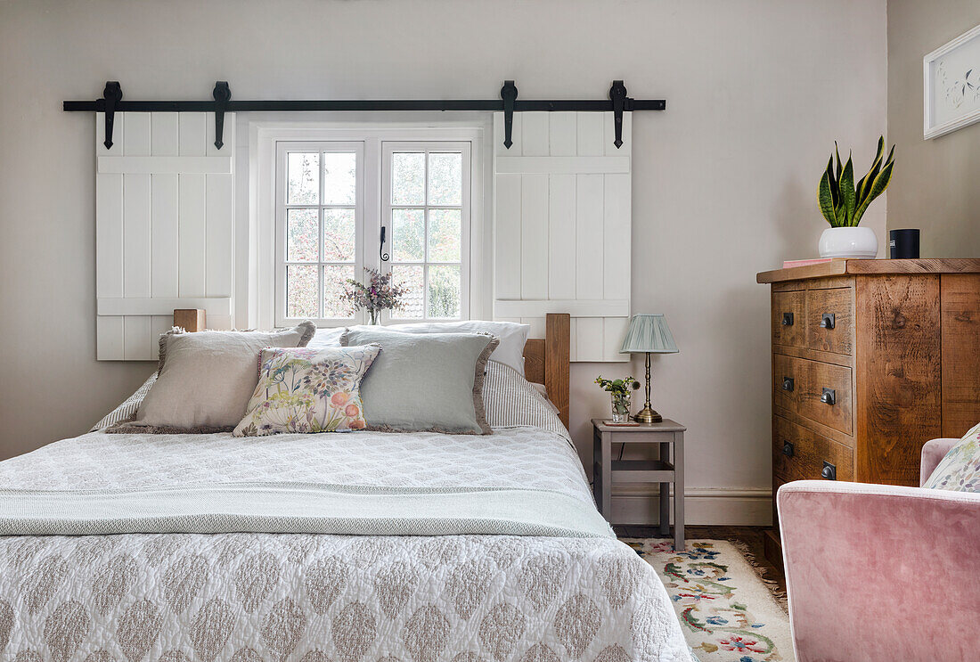 Doppelbett, eingerahmt von weiß gestrichenen Fensterläden und antike Kommode im Schlafzimmer