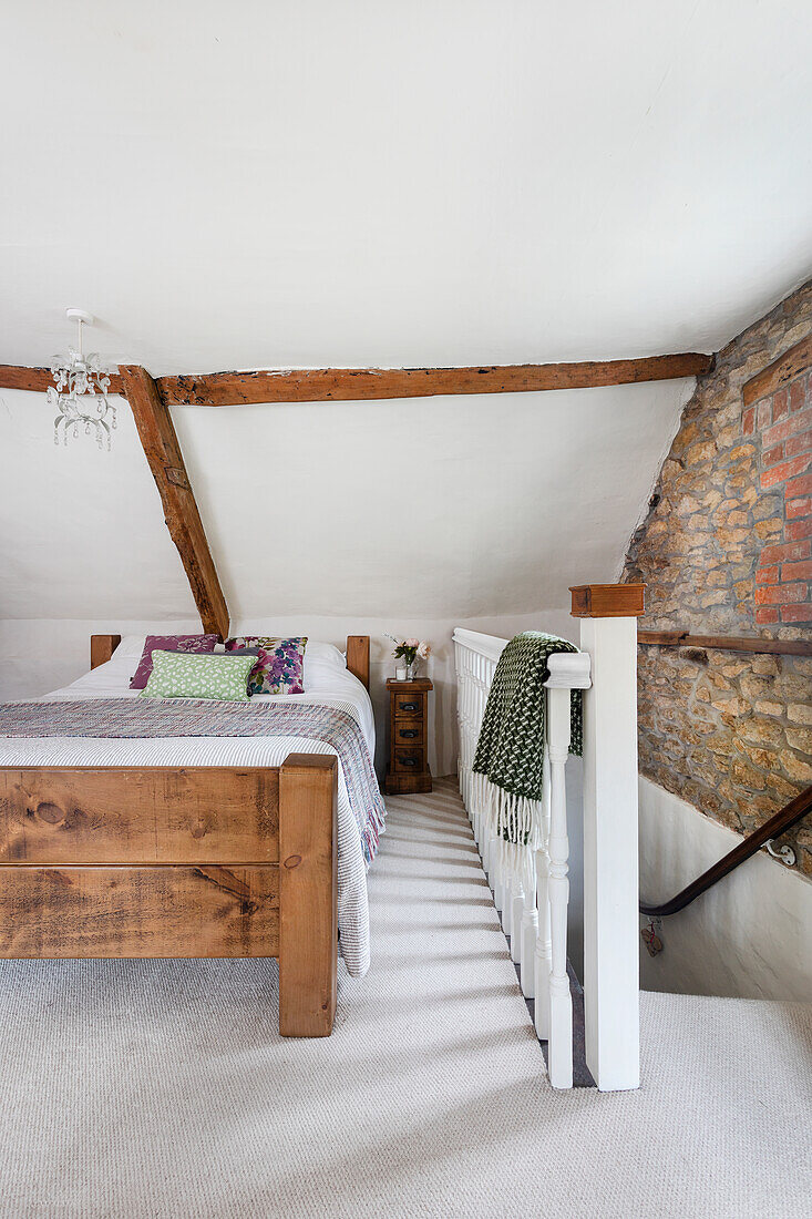 Doppelbett im Dachgeschoss-Schlafzimmer mit Holzbalken, Sichtmauerwerk und Treppenabgang