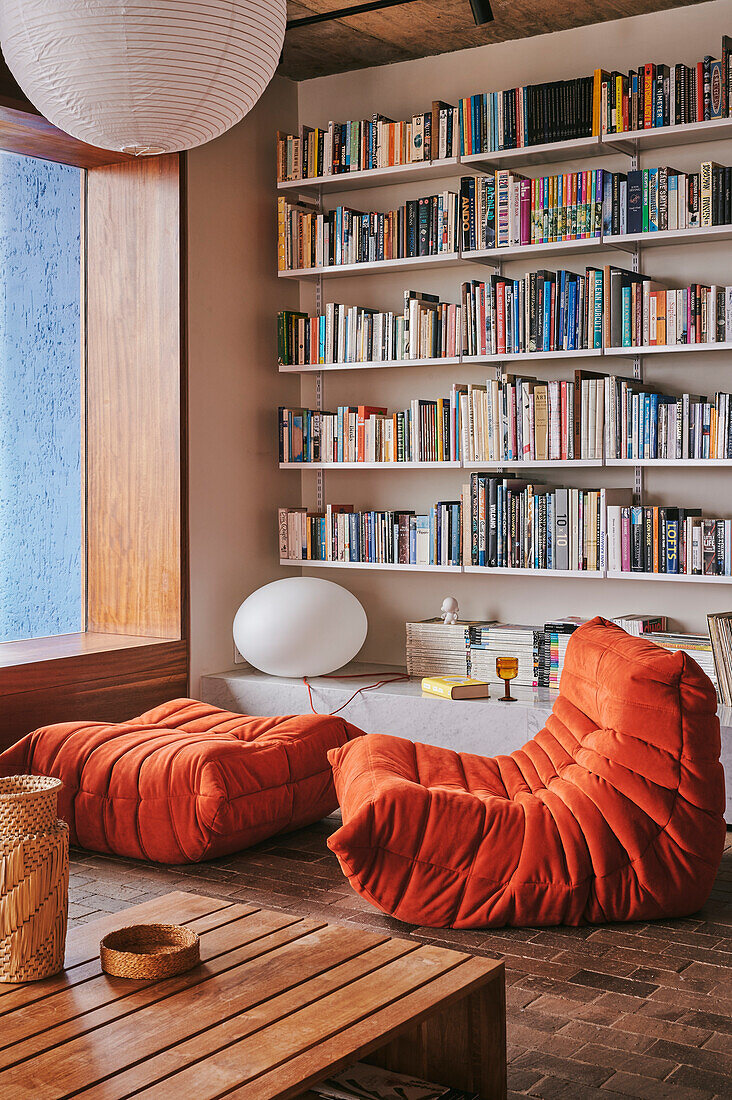 Orange-colored, cozy seating in front of a wall of bookshelves in a living room