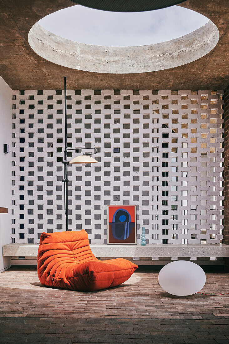 Orange-colored armchair and floor lamp in a living room with decorative concrete block wall and skylight