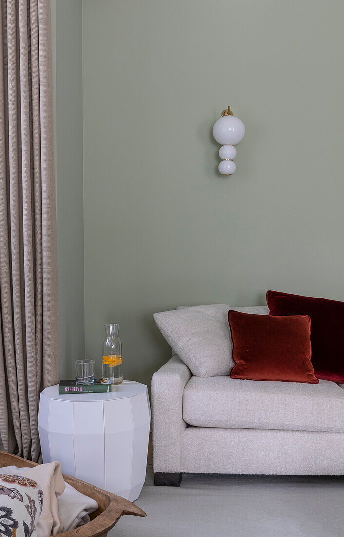White side table next to light-colored sofa with a light above on a green wall