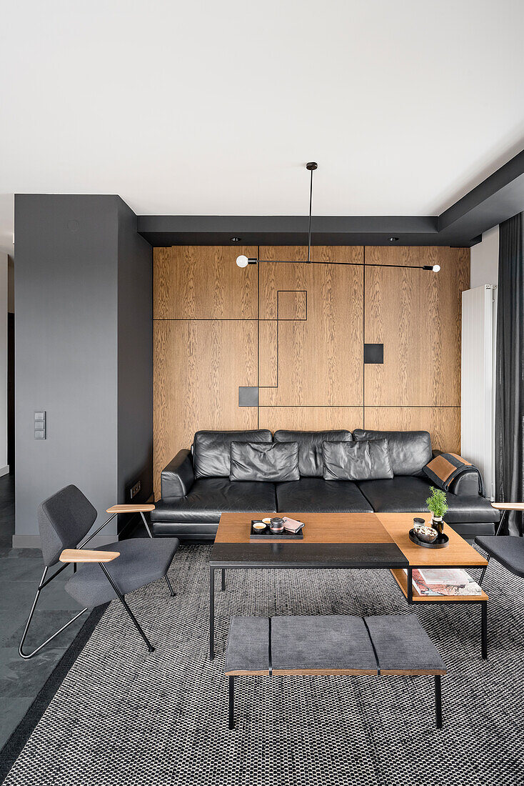 Living room in black and dark brown, wall above leather couch covered with oak veneer