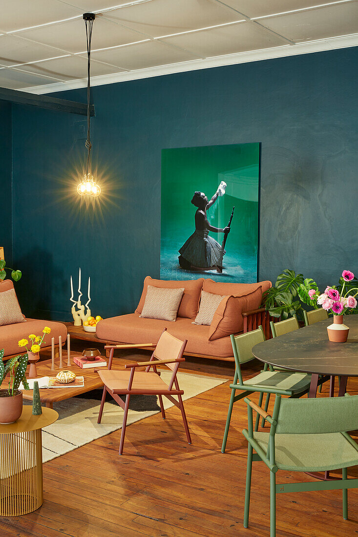 Sitzbereich mit braunem Sofa, grünen Stühlen und großem Bild an dunkelblauer Wand