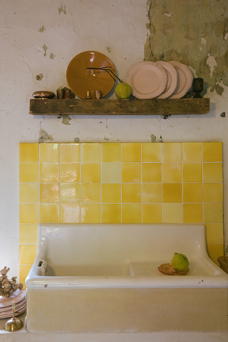 Vintage Spülbecken vor Wand mit gelben Fliesen, darüber Holzregal mit Tellern