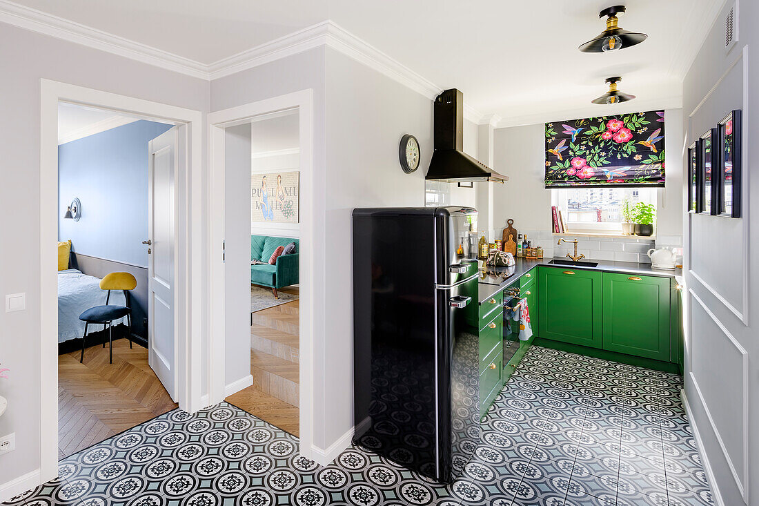 Dark green base cabinets, black refrigerator and geometric floor tiles in an open-plan kitchen