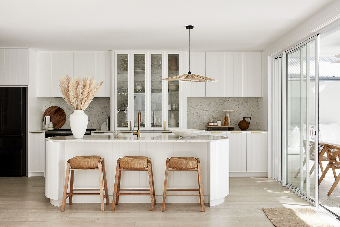 Modern coastal style kitchen with curved kitchen island, marble countertop, and rattan bar stools