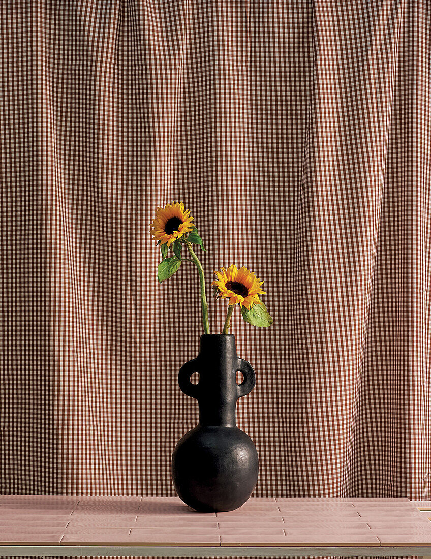 Sunflowers in a vase in front of a gingham curtain