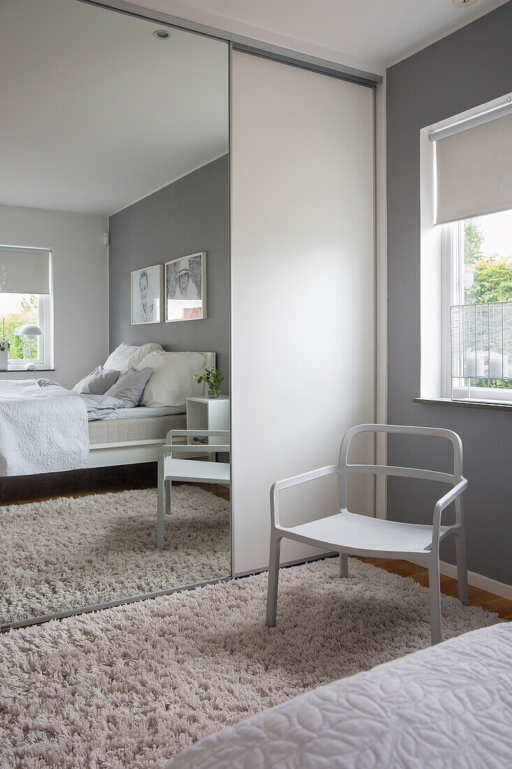 Floor-to-ceiling wardrobe with mirrored door, fluffy carpet and chair in a bedroom