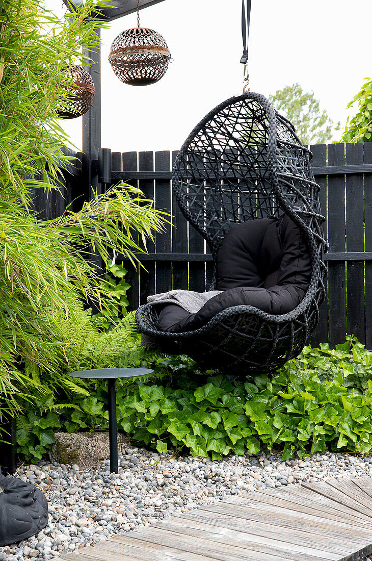 Black rattan hanging chair with cushions in the Asian-style garden area