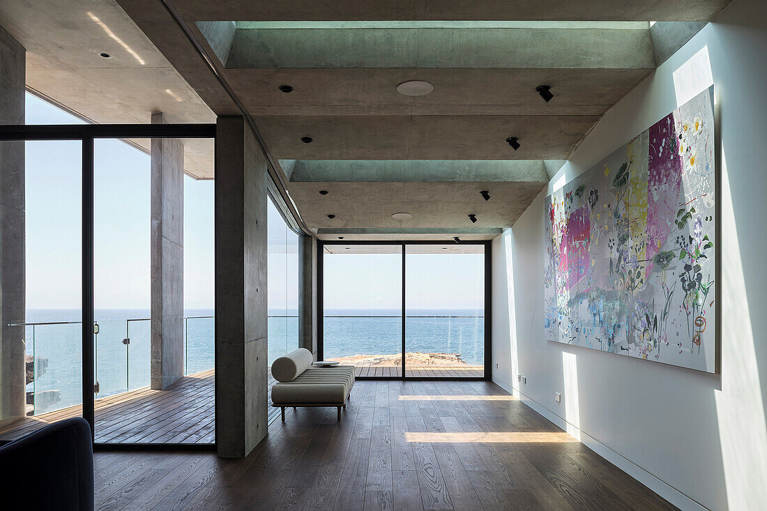 Minimalistischer Wohnraum mit Sofa und modernem Kunstwerk and der Wand, Blick auf das Meer