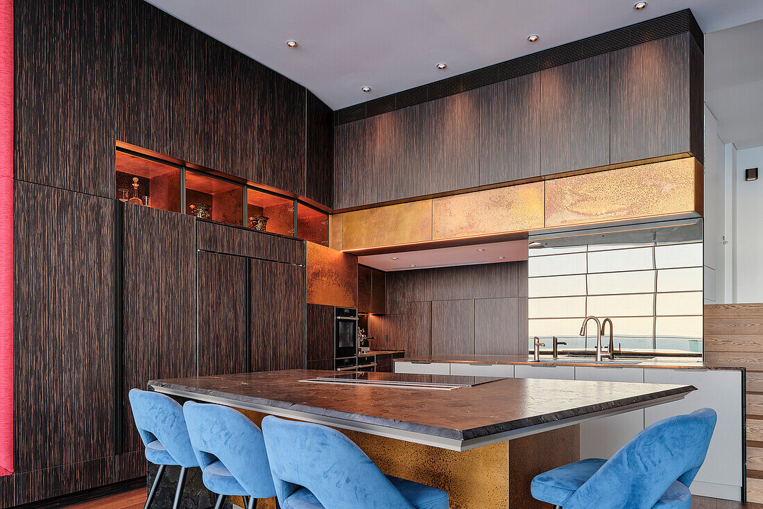 Custom-made kitchen with wooden cabinet fronts, dining table and blue upholstered chairs