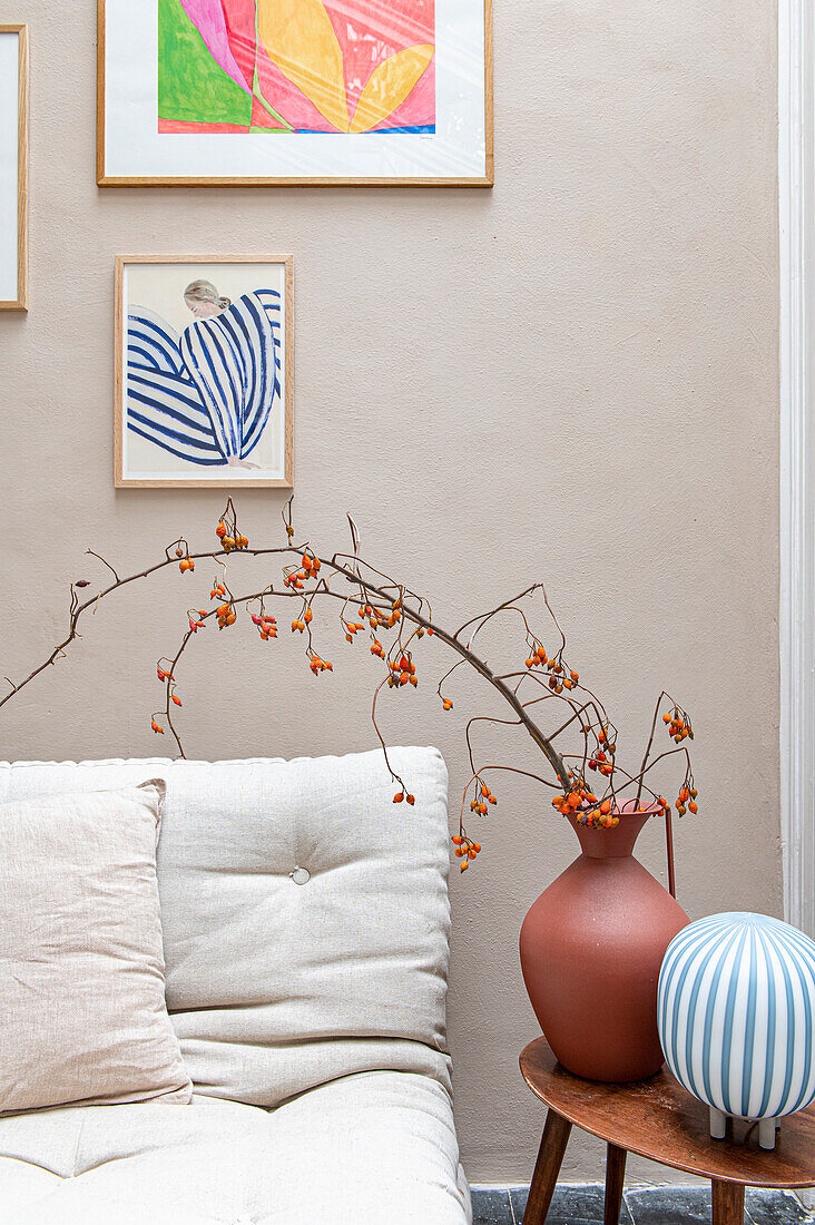 Vase with twigs and small orange berries next to cream-colored sofa