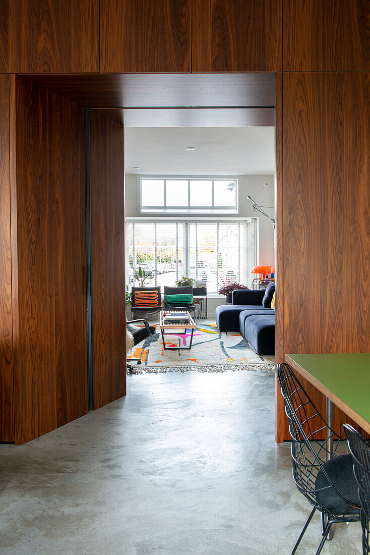 Passageway with wooden panelling to modern living room with concrete floor