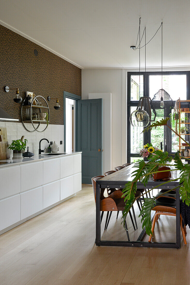 Modern kitchen with grey table, designer chairs and hanging lamps in front of floor-to-ceiling windows