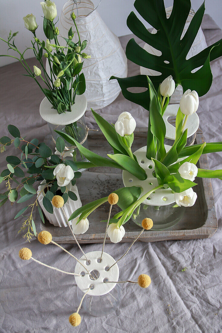 Flowers and leaves in vases with homemade lid on wooden tray and linen tablecloth