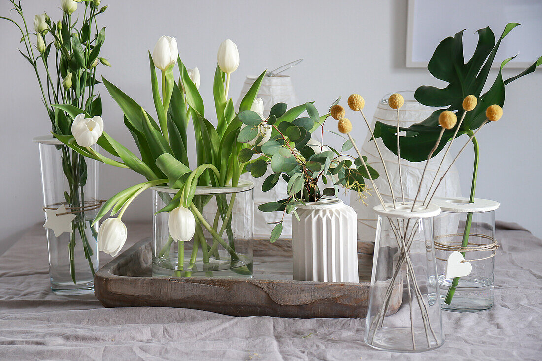 Vases with flowers and plants on tray and linen tablecloth