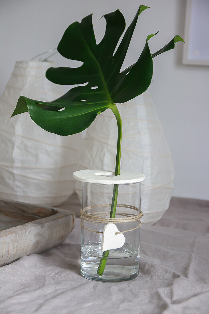 Monstera leaf in simple glass jar with homemade lid and pendant on linen tablecloth