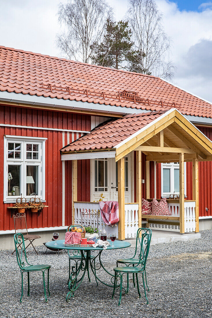 Rotes Holzhaus mit überdachtem Eingang und grüner Sitzgruppe im Vorgarten