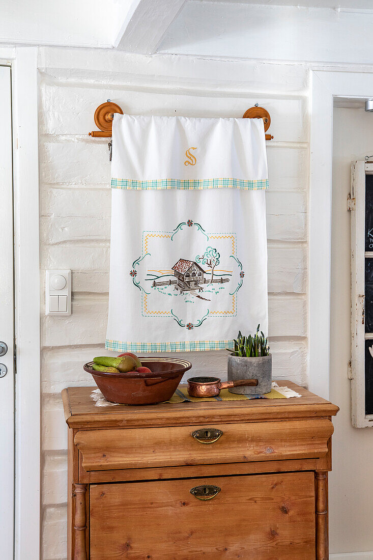 Wall hanging with embroidery above antique wooden chest of drawers