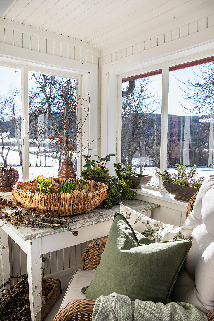 Entrance hall with table, woven basket, armchair and plants on a white windowsill