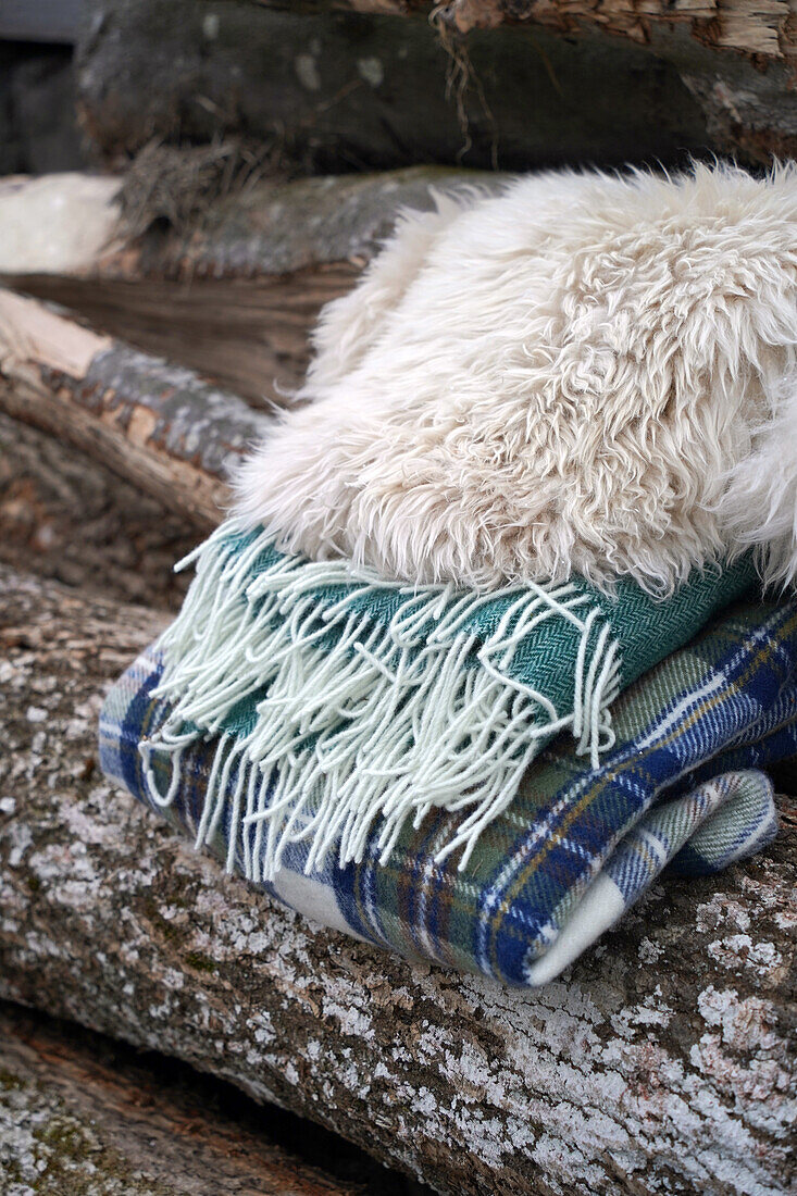 Wolldecken und Schaffell liegen auf einem Holzstapel, Decken für einen Sitzplatz im Winter im Freien