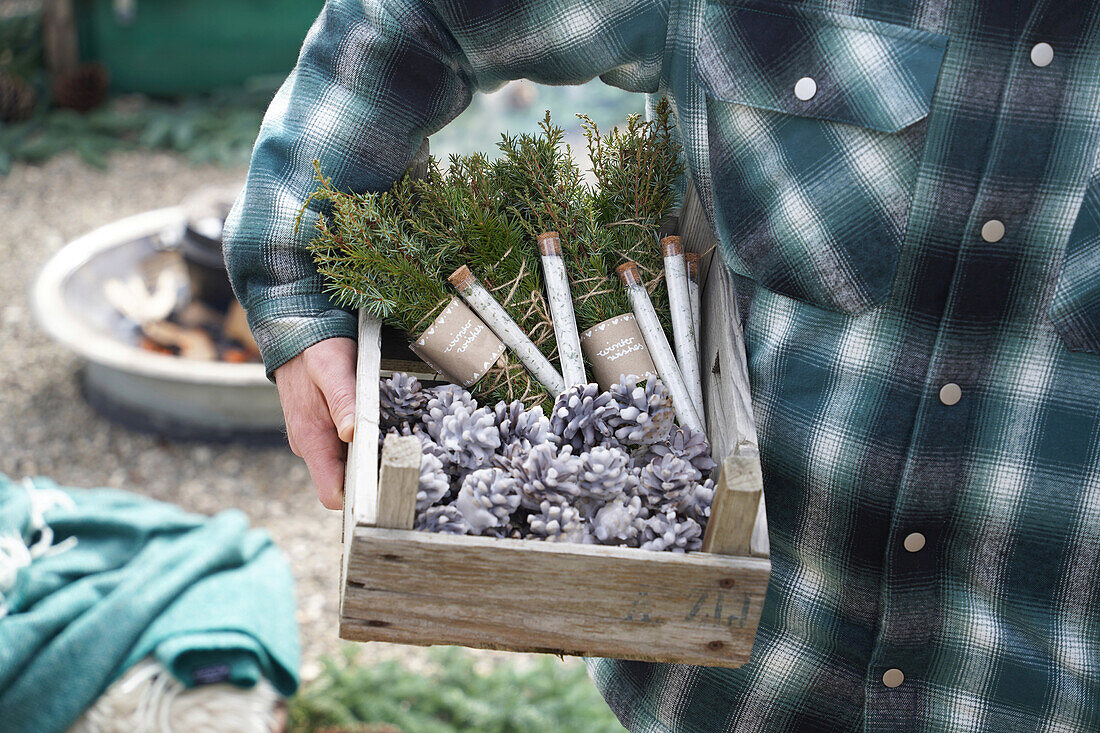 Man carrying wooden box with DIYs, pinecone fire starters, bundles of incense made from juniper and spruce branches, spruce salt in test tubes