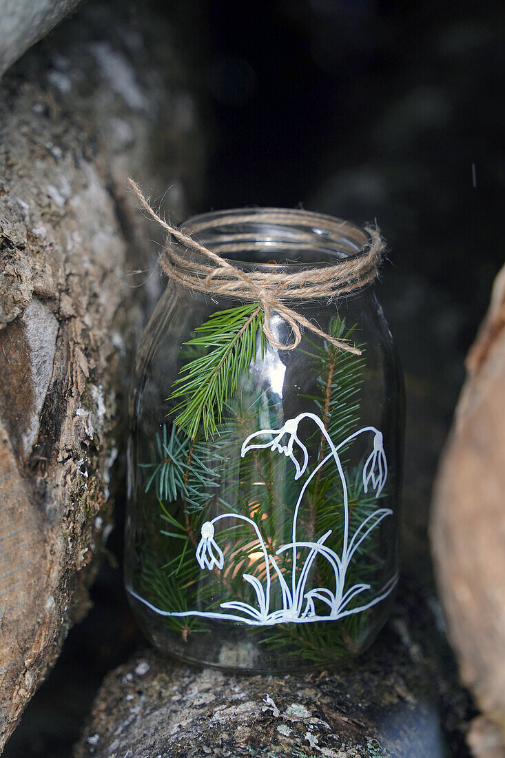 DIY Altes Glas bemalt mit Schneeglöckchenmotiv (Kreidestift)  dekoriert mit Fichtenzweigen und Schnur, Windlicht, auf einem Holzstamm