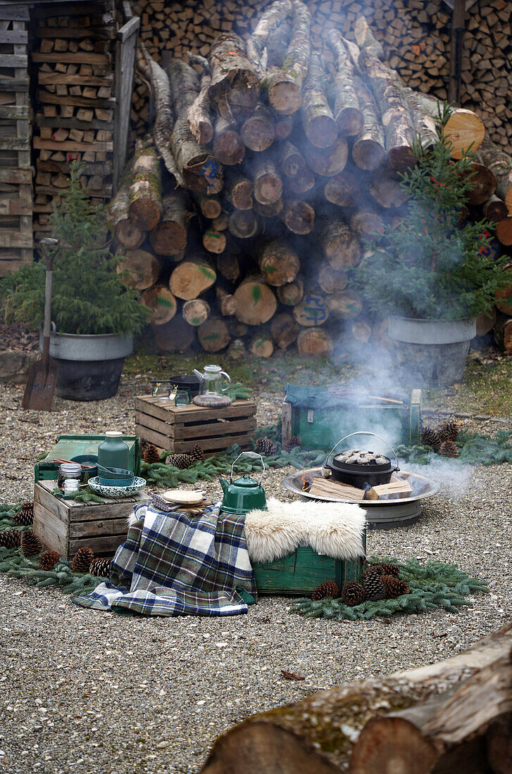 Barbecue area with wooden boxes to sit on with Dutch ovens in the fire pit, surrounded by firewood, campfire site, rustic ambience