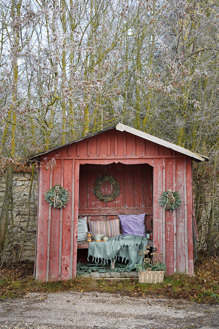 Rotes Holzhaus mit Decken, Kissen und selbstgemachten Kränzen