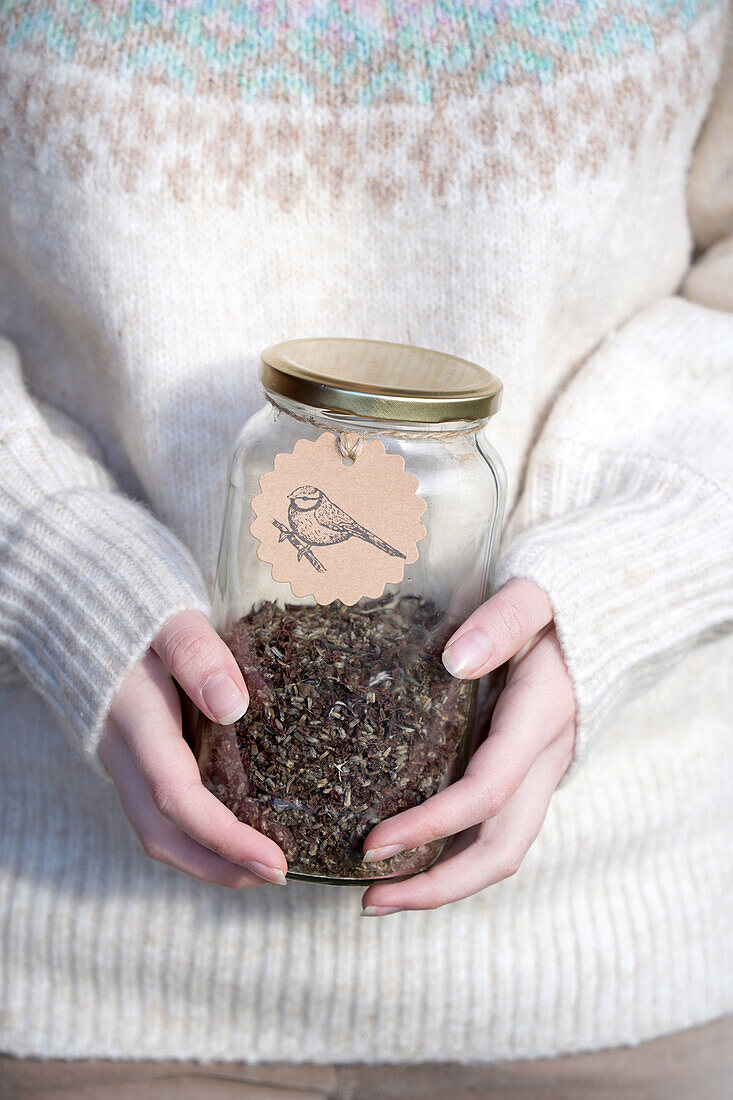 Glass jar with bird food and bird motif label held in hands