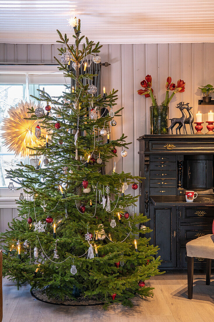 Weihnachtlich geschmückter Baum mit Kerzenlicht im Wohnzimmer