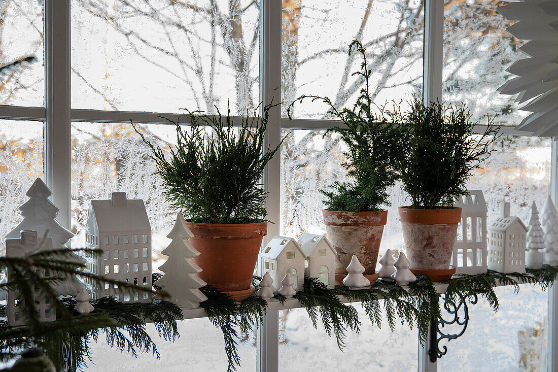 Winter window decoration with fir greenery and ceramic house