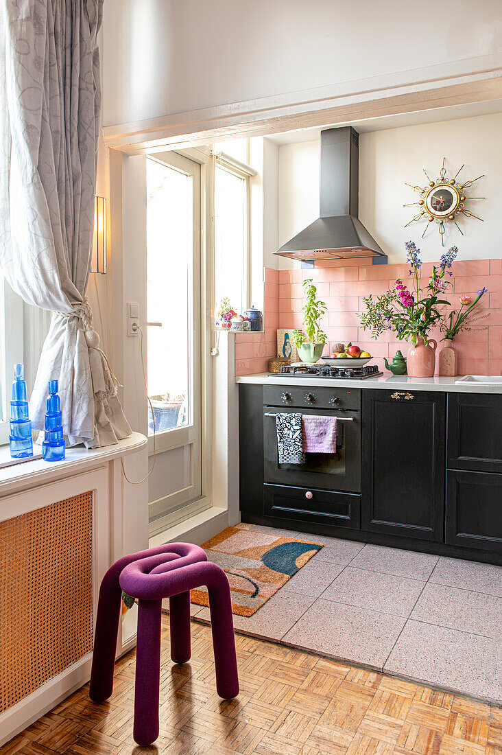 Kitchen with pink tiles, black cupboards and abstract stool