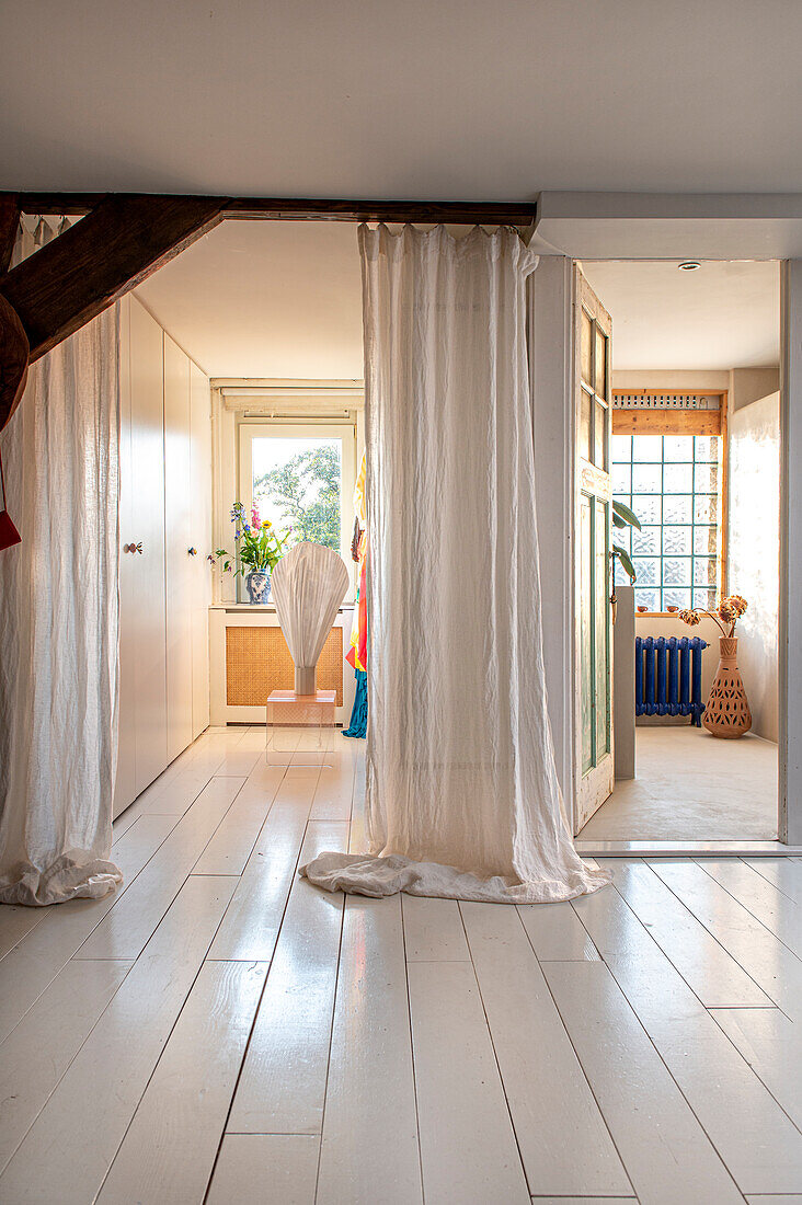 Raum mit weißen Holzdielen und Vorhängen, Blick in andere Zimmer