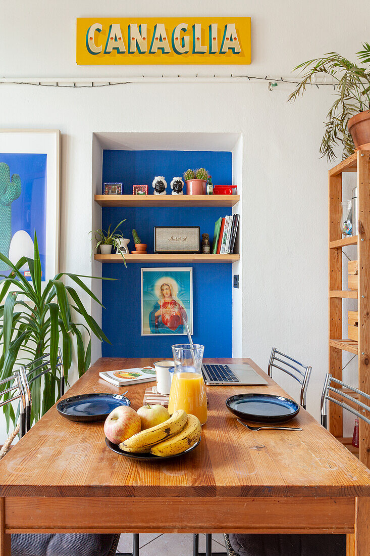 Gedeckter Esstisch mit Obstschale, blaue Wand und Regale